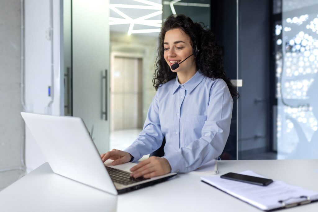 Successful hispanic woman with headset phone for video call working with laptop while sitting at